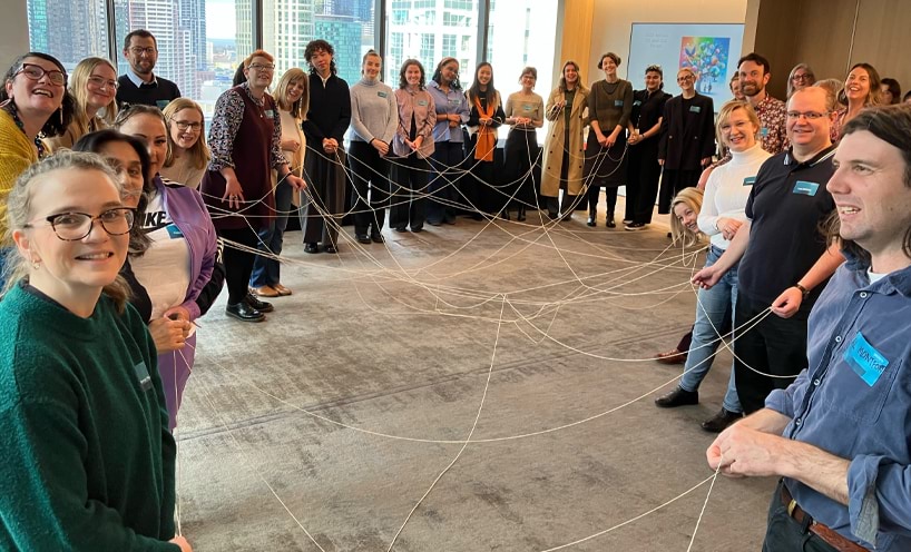Participants at the forum are standing in a circle and each holding a section of string. There are many strings crossing over in the centre.